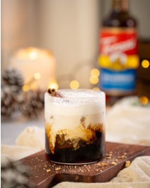 Gingerbread White Russian on a cutting board in front of pine cones, a candle, and a syrup bottle.